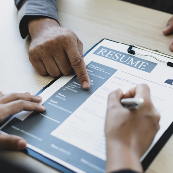A hand points at a resume as another person's hands make notes on it with a pen