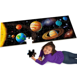A young girl lies on the floor, placing a puzzle piece into a large floor puzzle depicting the solar system.